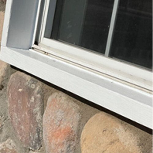 A white window is sitting on a stone wall.