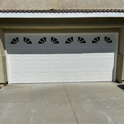 A white garage door with a fan design on it is sitting on top of a concrete driveway.