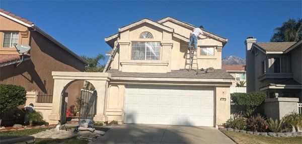 A man on a ladder is painting the side of a house.