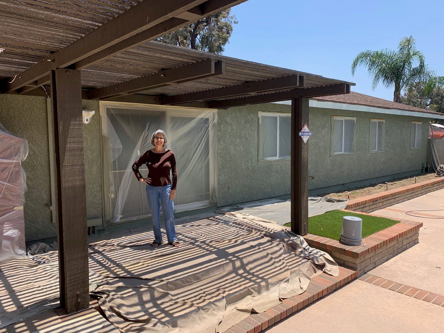 A woman is standing under a pergola in front of a house.