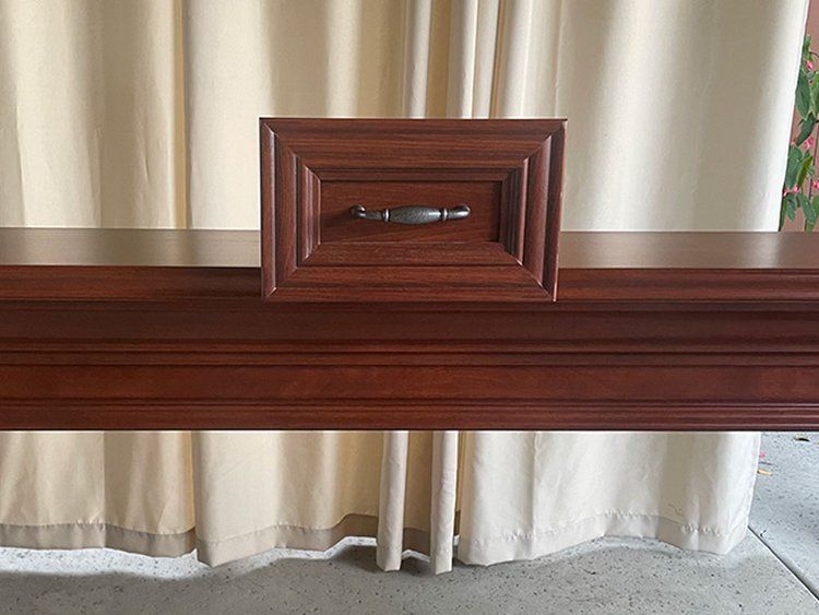 A wooden table with a drawer underneath it in front of a white curtain.