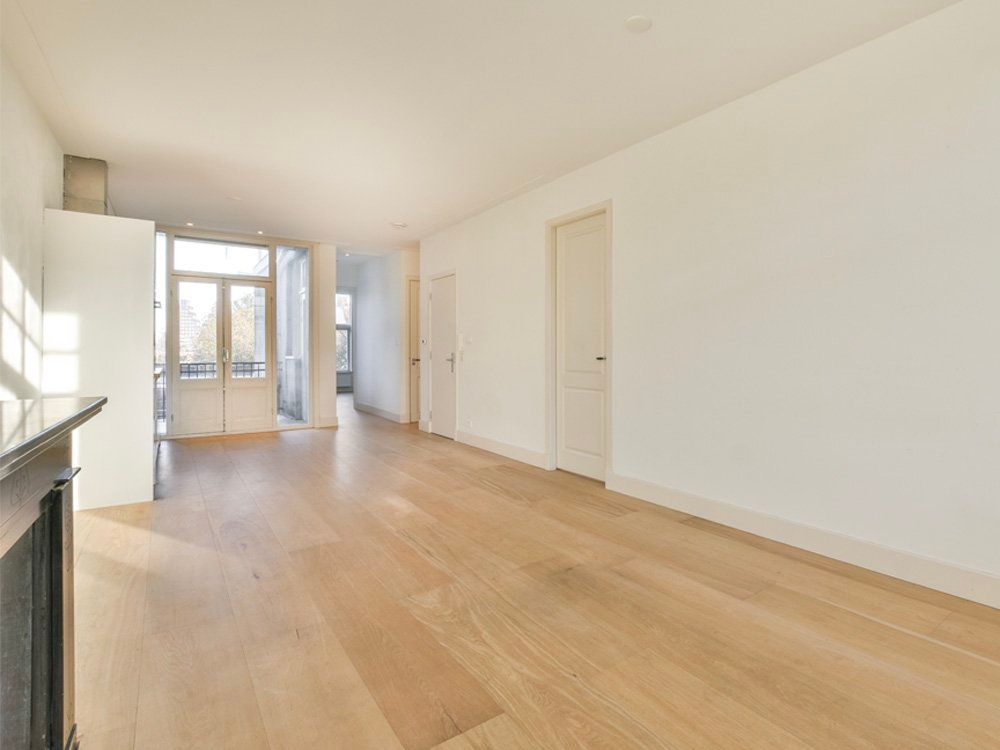 An empty living room with hardwood floors and white walls.