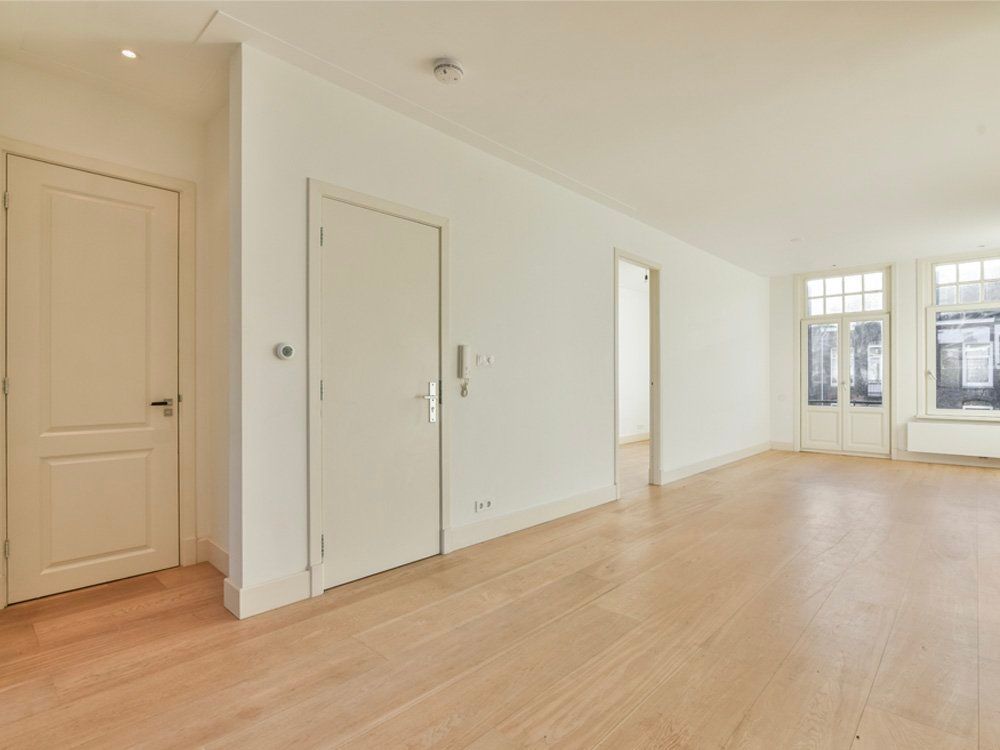 An empty living room with hardwood floors and white walls.