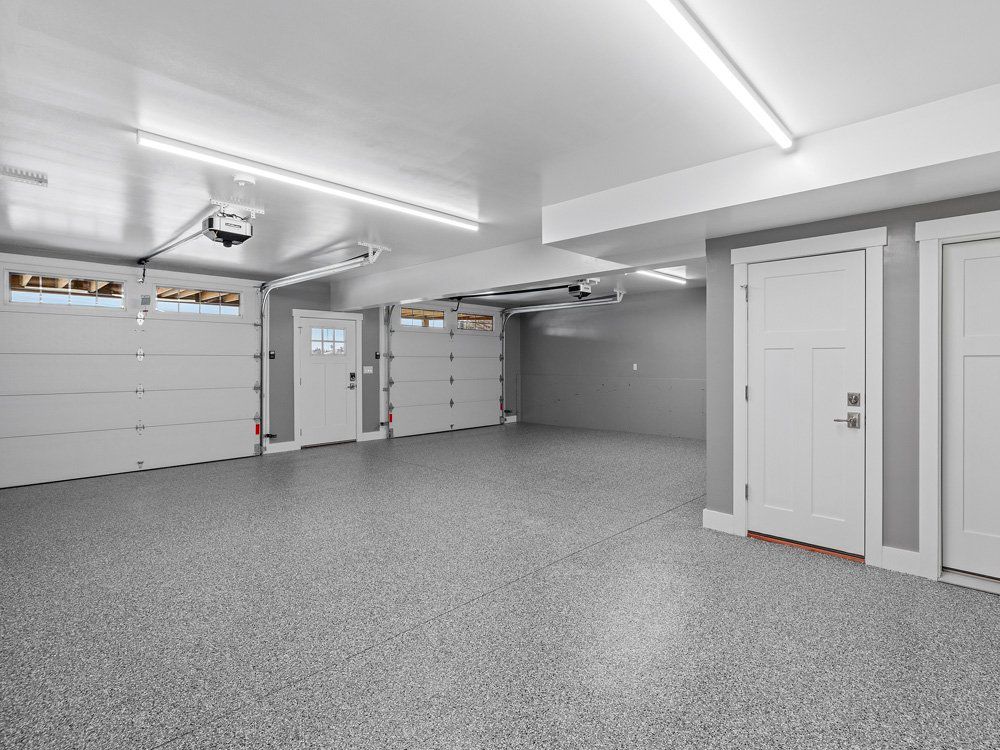 An empty garage with two garage doors and a gray floor.