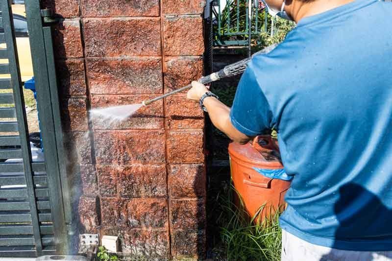 A man is cleaning a brick wall with a high-pressure washer.