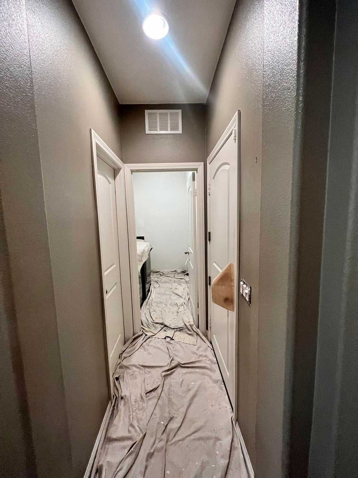 A long hallway with a white sheet on the floor leading to a bathroom.