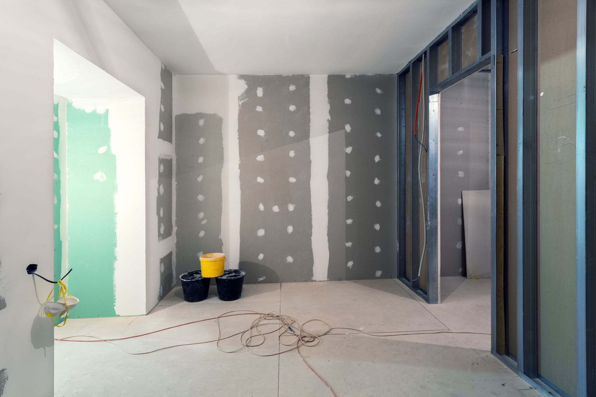 An empty room with drywall walls and a yellow bucket on the floor