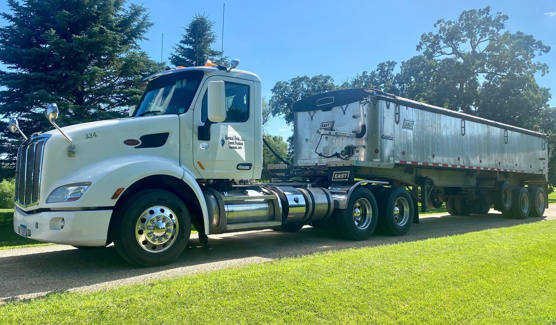 white semi-truck and trailer parked on a grassy area with trees in the background on a sunny day
