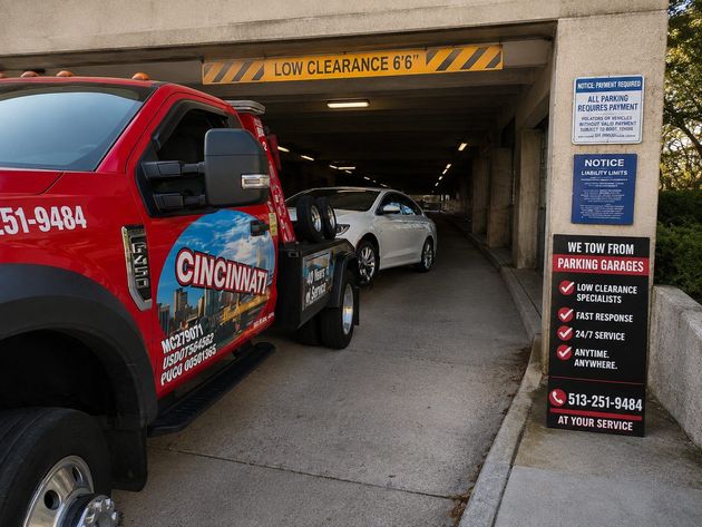 Red tow truck with Cincinnati branding towing a white car from a low-clearance garage entrance