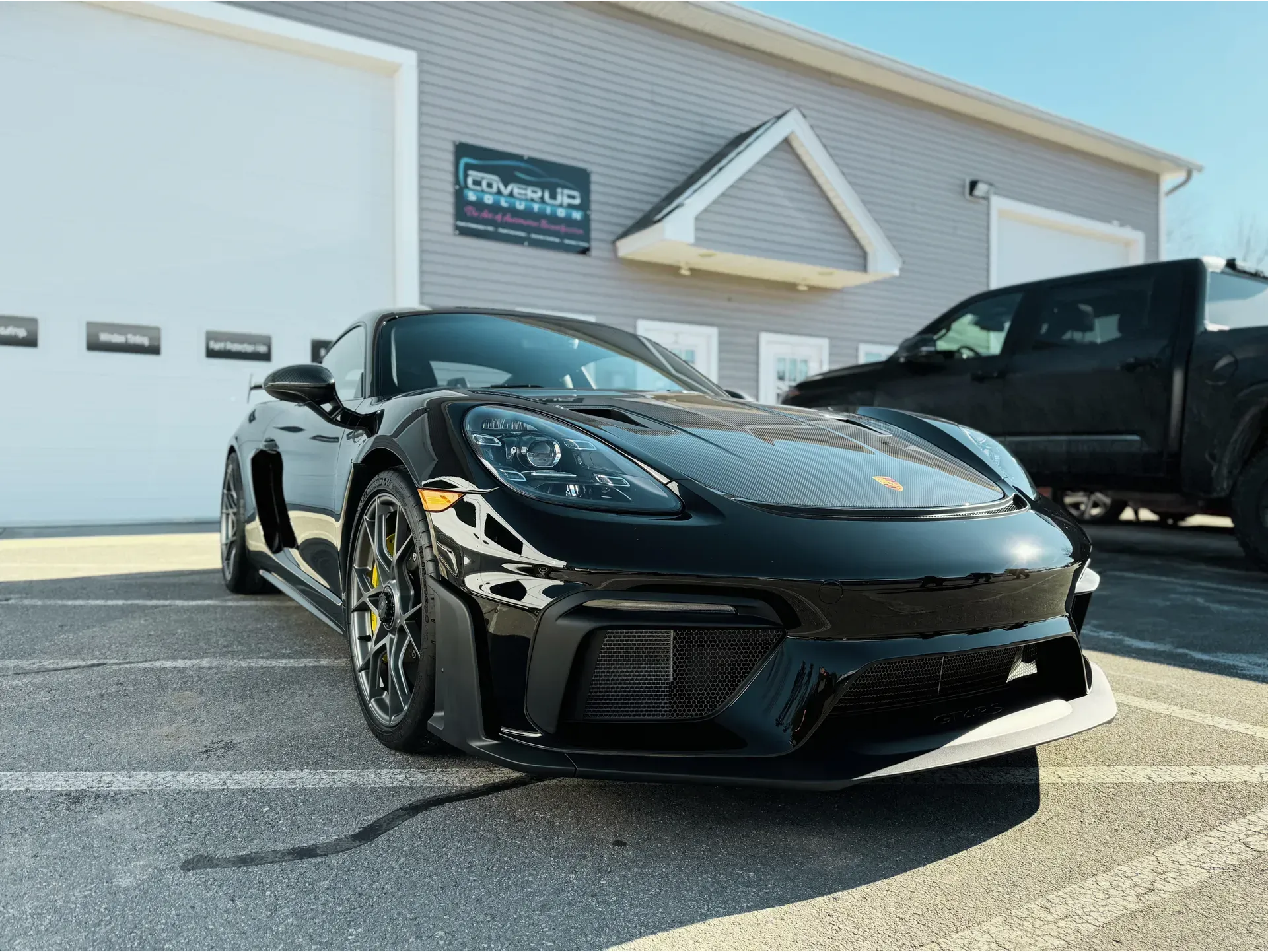 A shiny black Porsche sports car parked in front of a light-gray building on a sunny day.