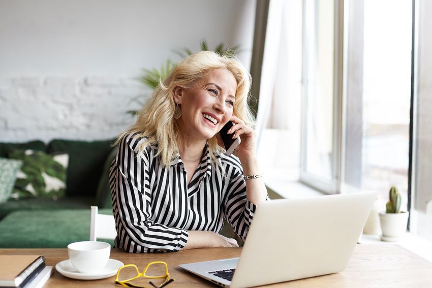 A woman is sitting at a desk with a laptop and talking on a cell phone.