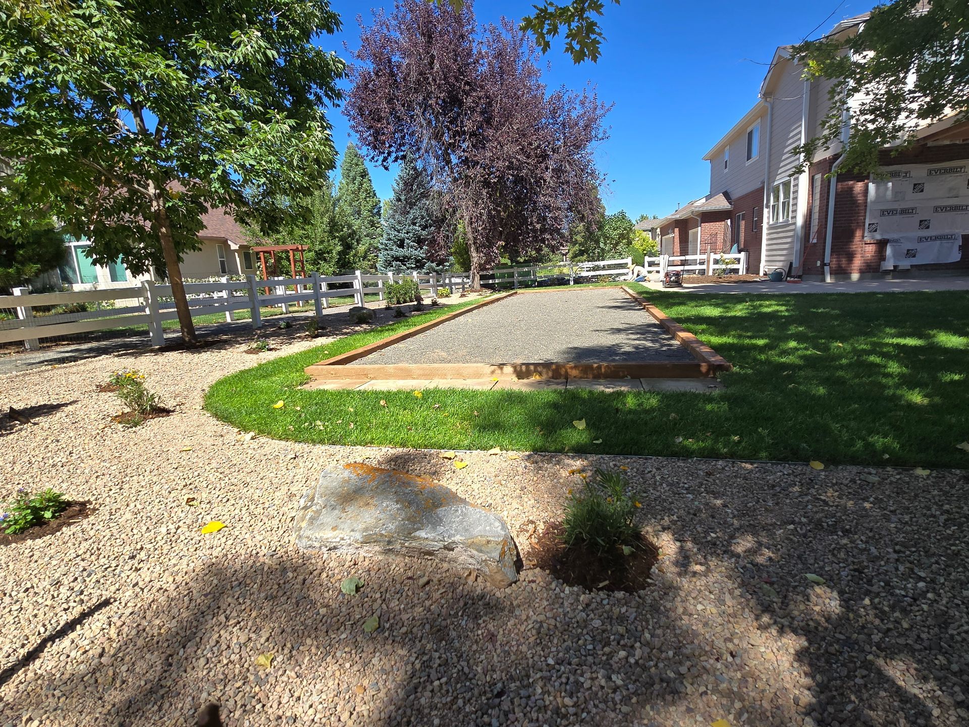 A gravel driveway leading to a house with a white fence