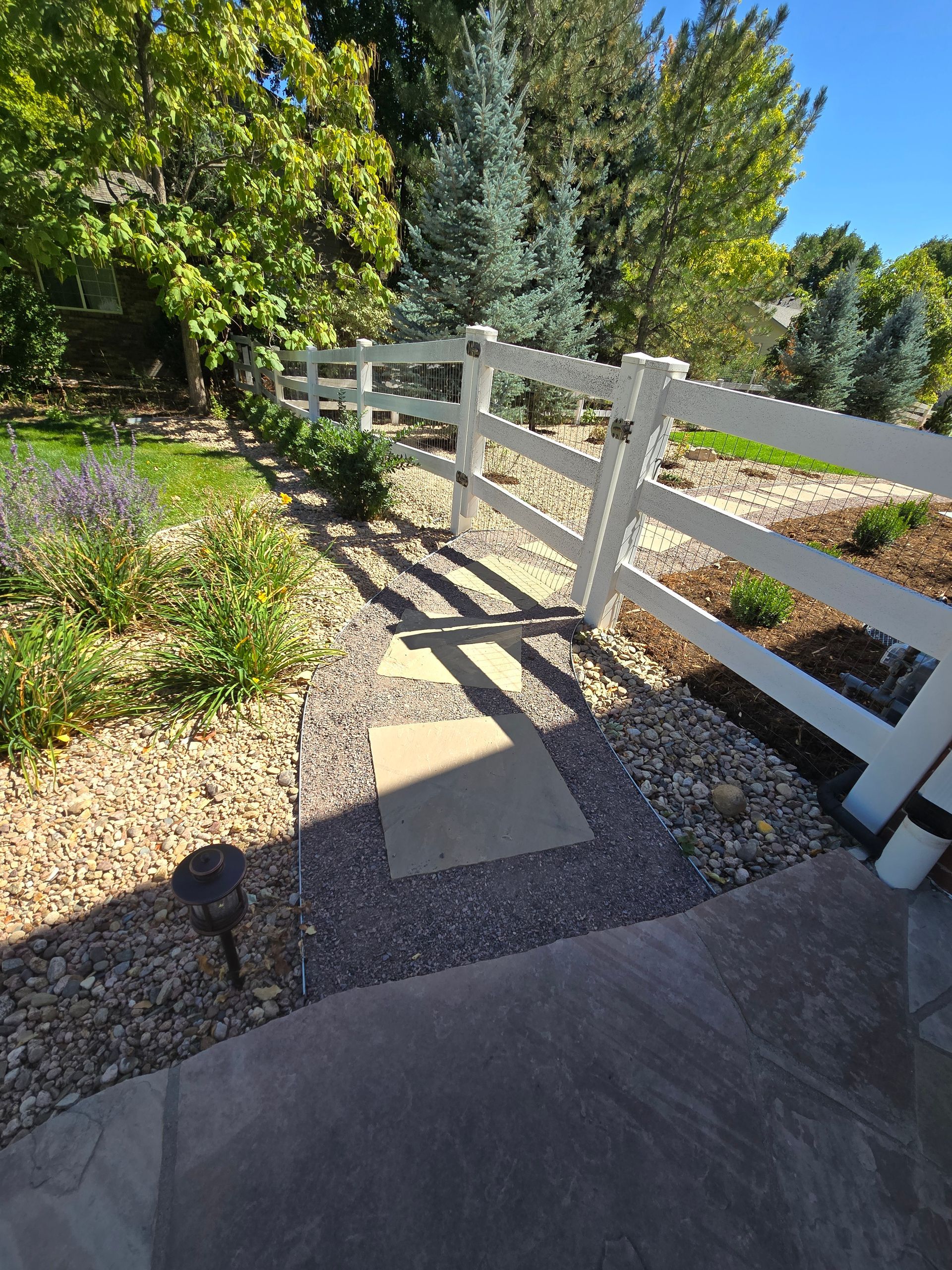 A white fence surrounds a gravel path in a yard