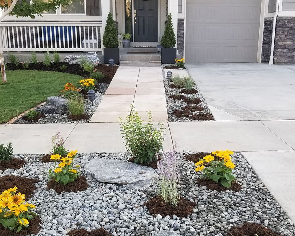 A walkway leading to a house with flowers and rocks in front of it.