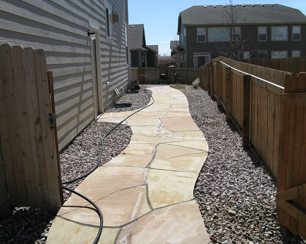 A stone walkway leading to a house with a wooden fence