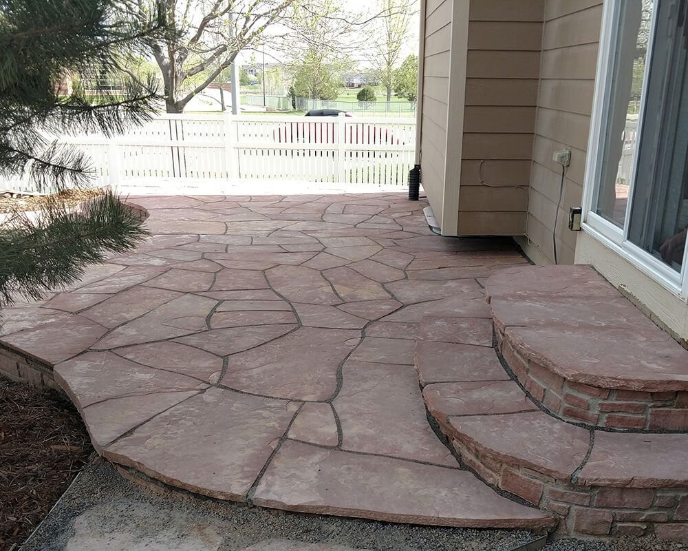 A stone patio with stairs leading up to it in front of a house.