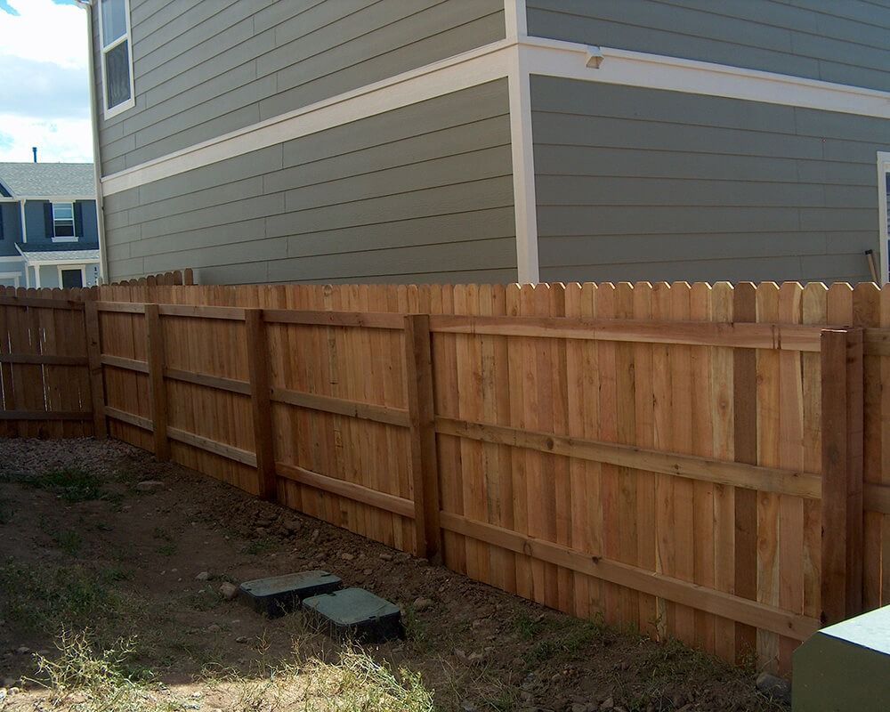 A wooden fence surrounds the backyard of a house