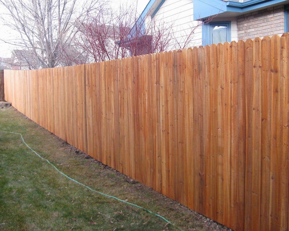 A wooden fence surrounds a lush green yard in front of a house.