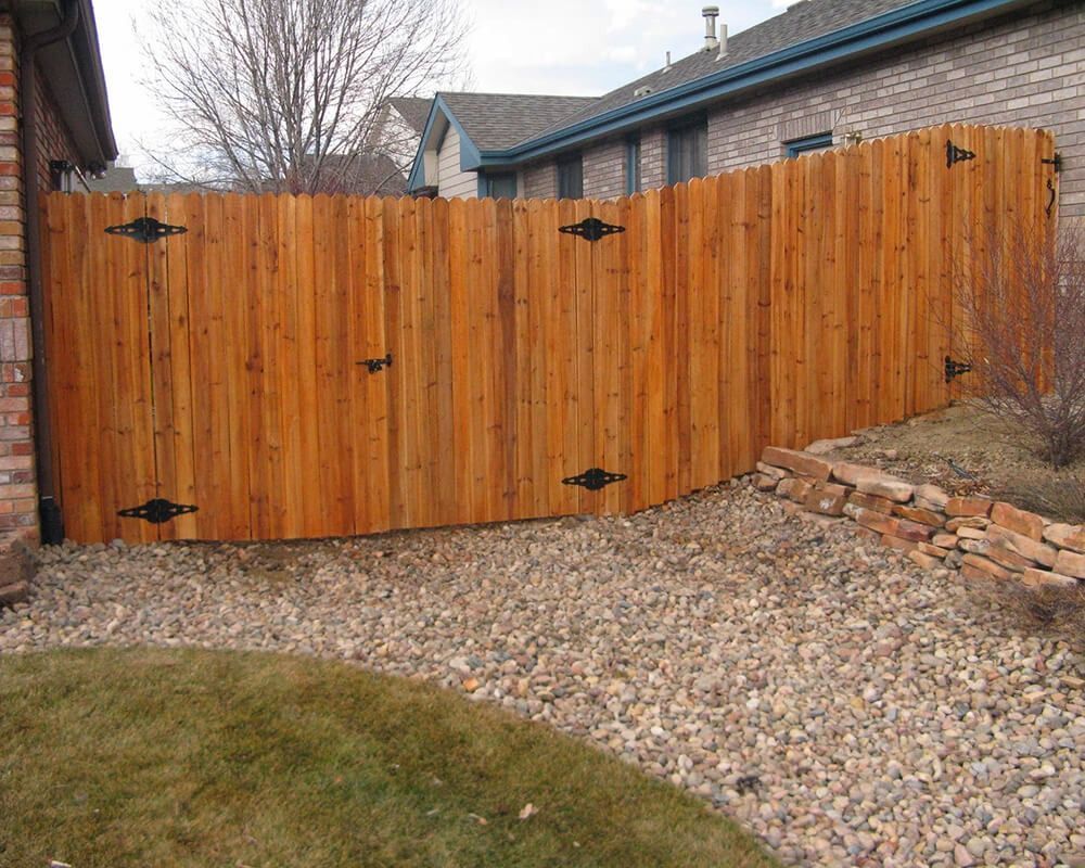 A wooden fence surrounds a gravel driveway in front of a brick house.