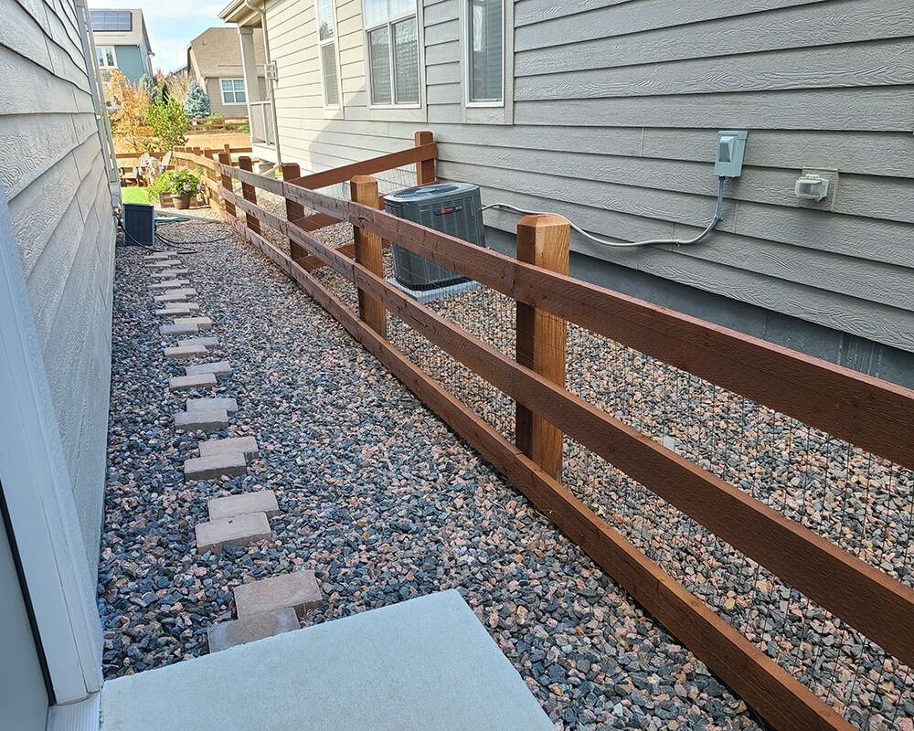 A wooden fence surrounds a gravel path leading to a house.