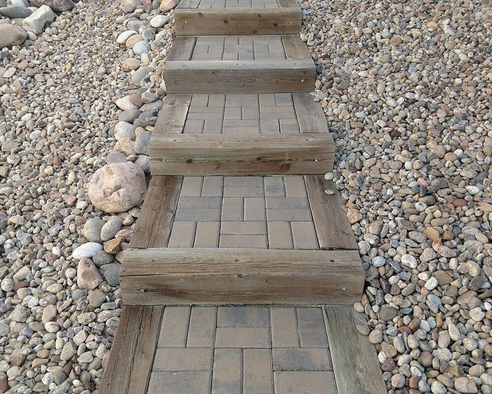 A brick walkway with wooden steps leading up to a pile of rocks.