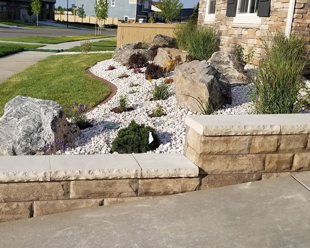 A brick wall surrounds a rock garden in front of a house.