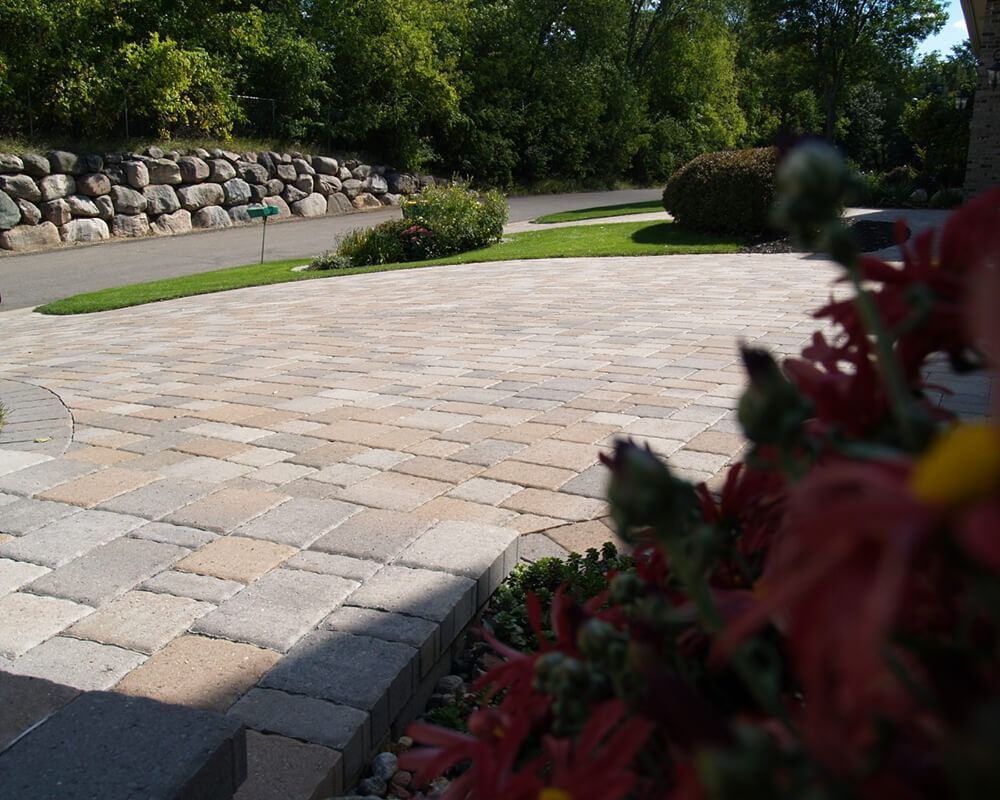 A driveway with flowers in the foreground and trees in the background