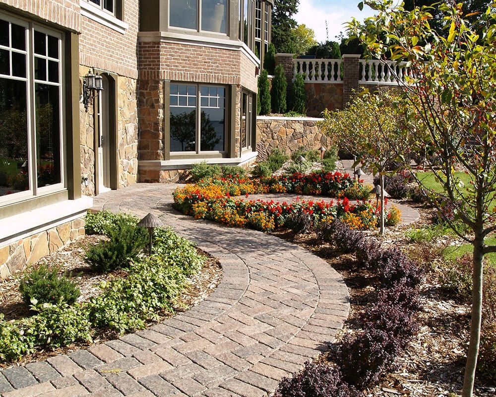 A brick walkway leading to a house surrounded by flowers