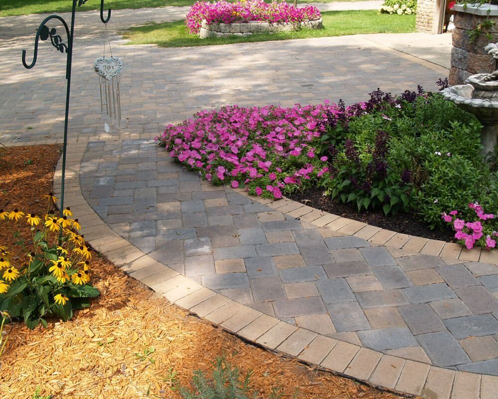 A brick walkway surrounded by flowers and a fountain