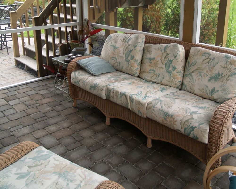 A screened in porch with a wicker couch and ottoman