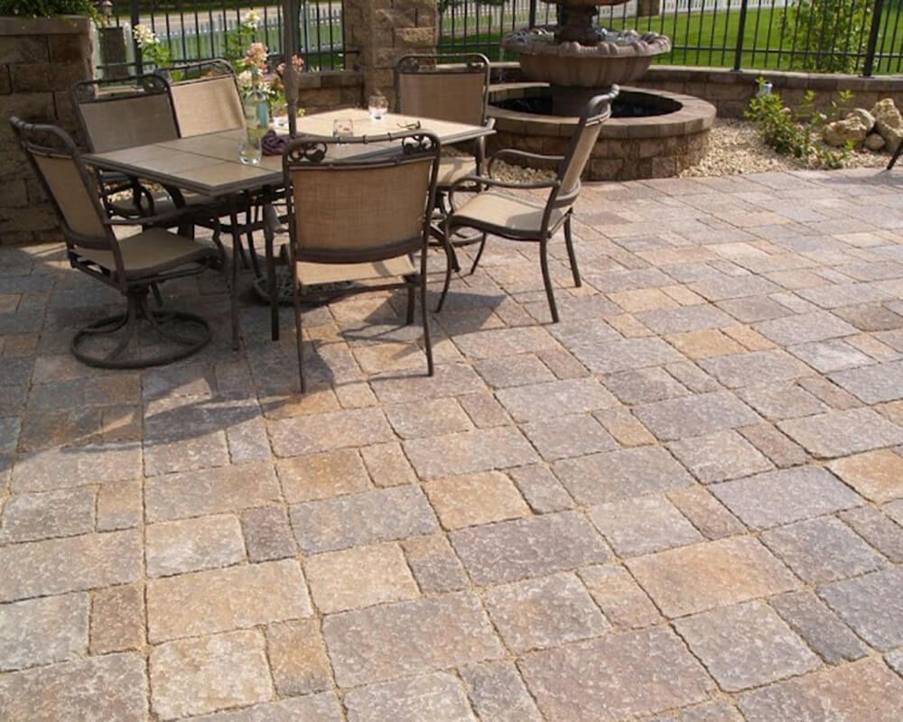 A patio with a table and chairs and a fountain in the background