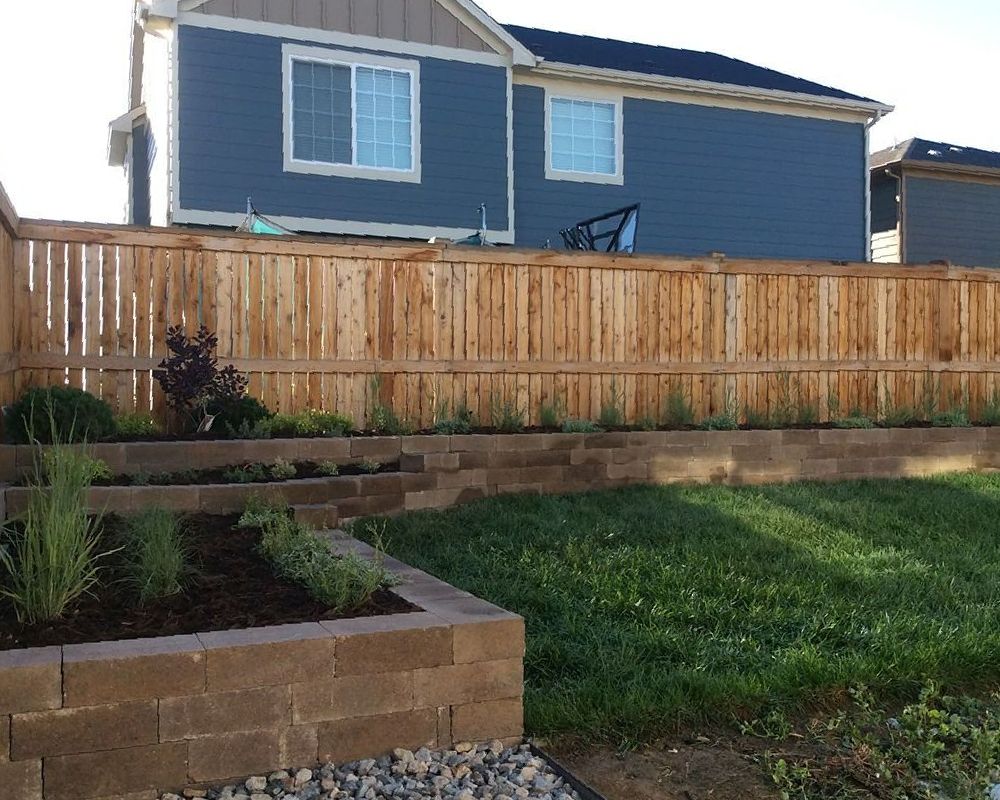 A wooden fence surrounds a garden in front of a house.