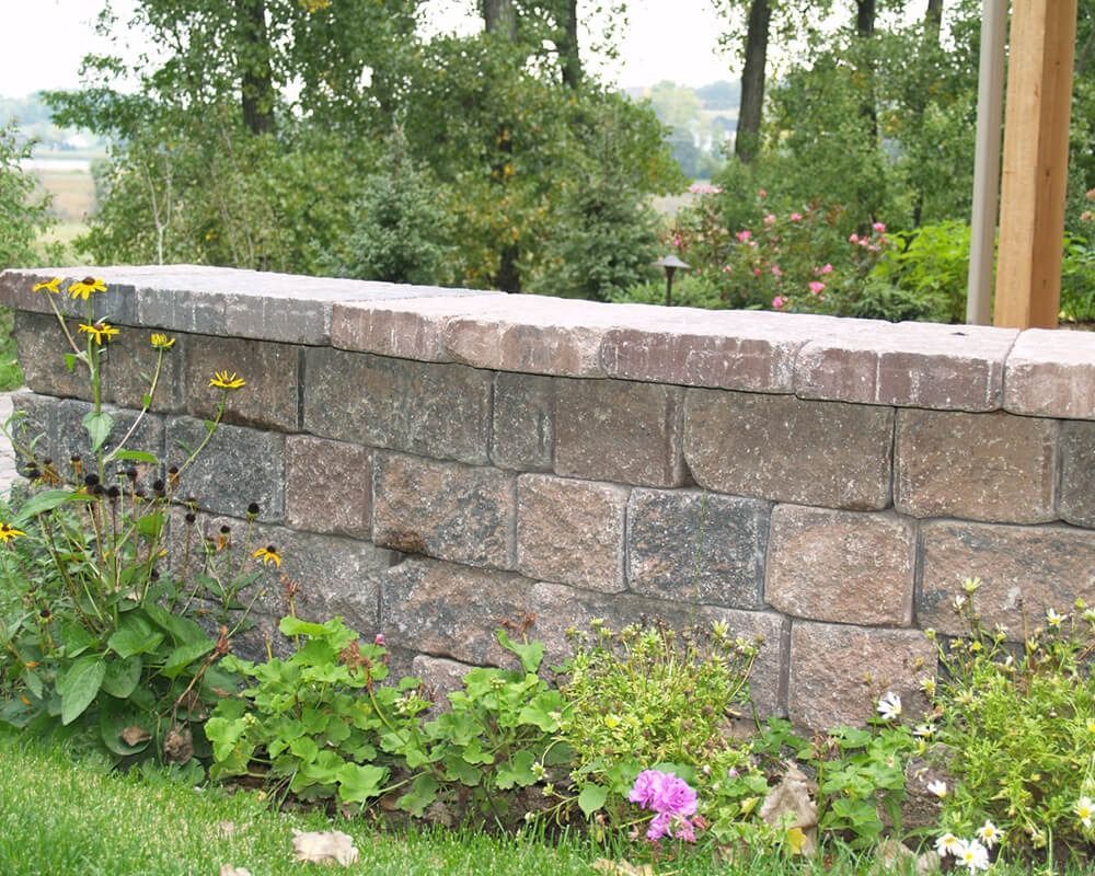 A stone wall in a garden with flowers and trees in the background