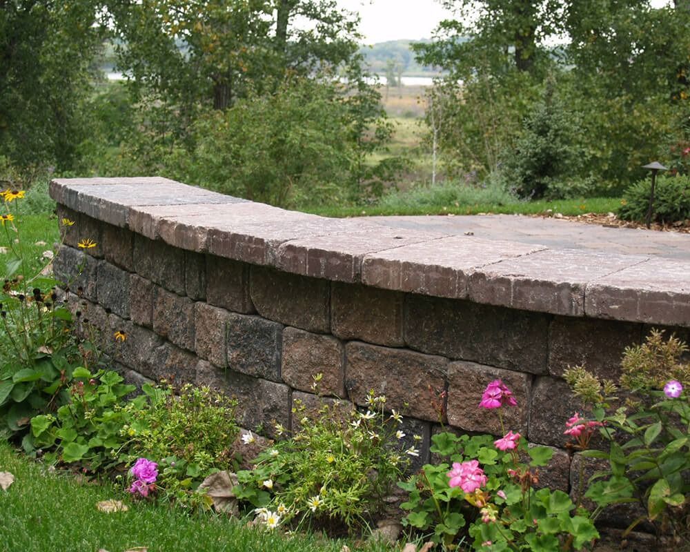 A stone wall with flowers and trees in the background