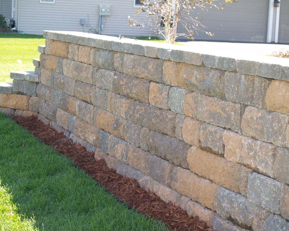 A stone wall surrounds a lush green lawn in front of a house.