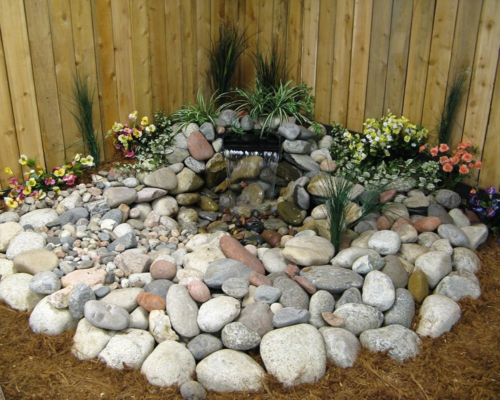 A garden with rocks and flowers in front of a wooden fence