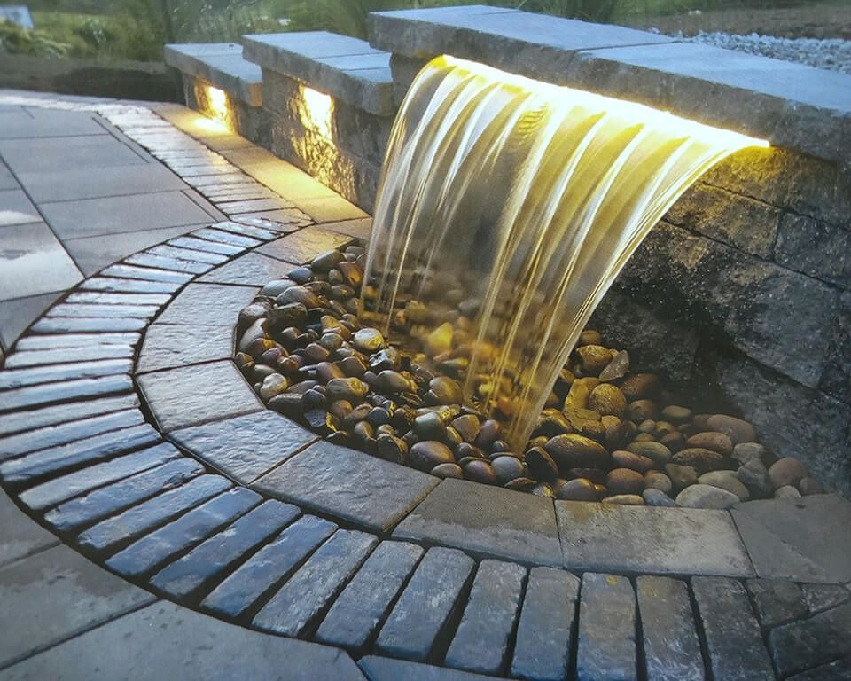 A waterfall is surrounded by bricks and rocks and is lit up at night
