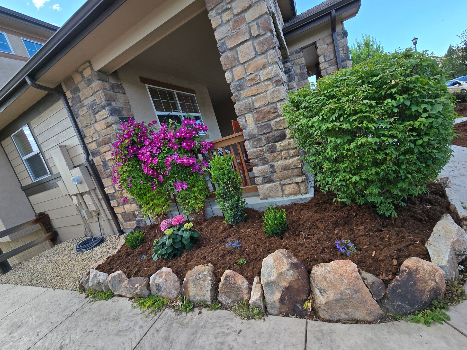 A house with purple flowers and rocks in front of it.