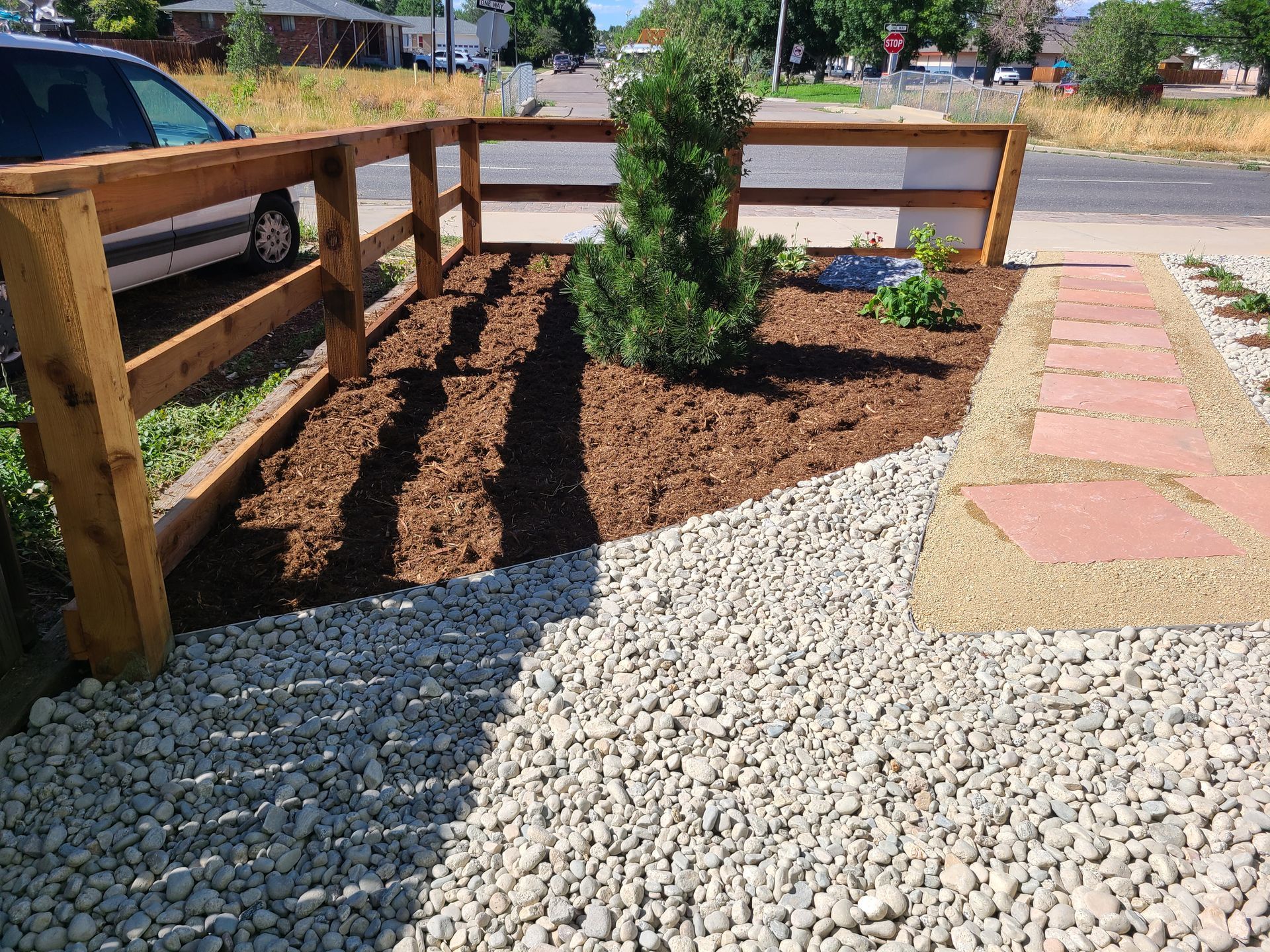 A wooden fence is surrounded by gravel and a tree