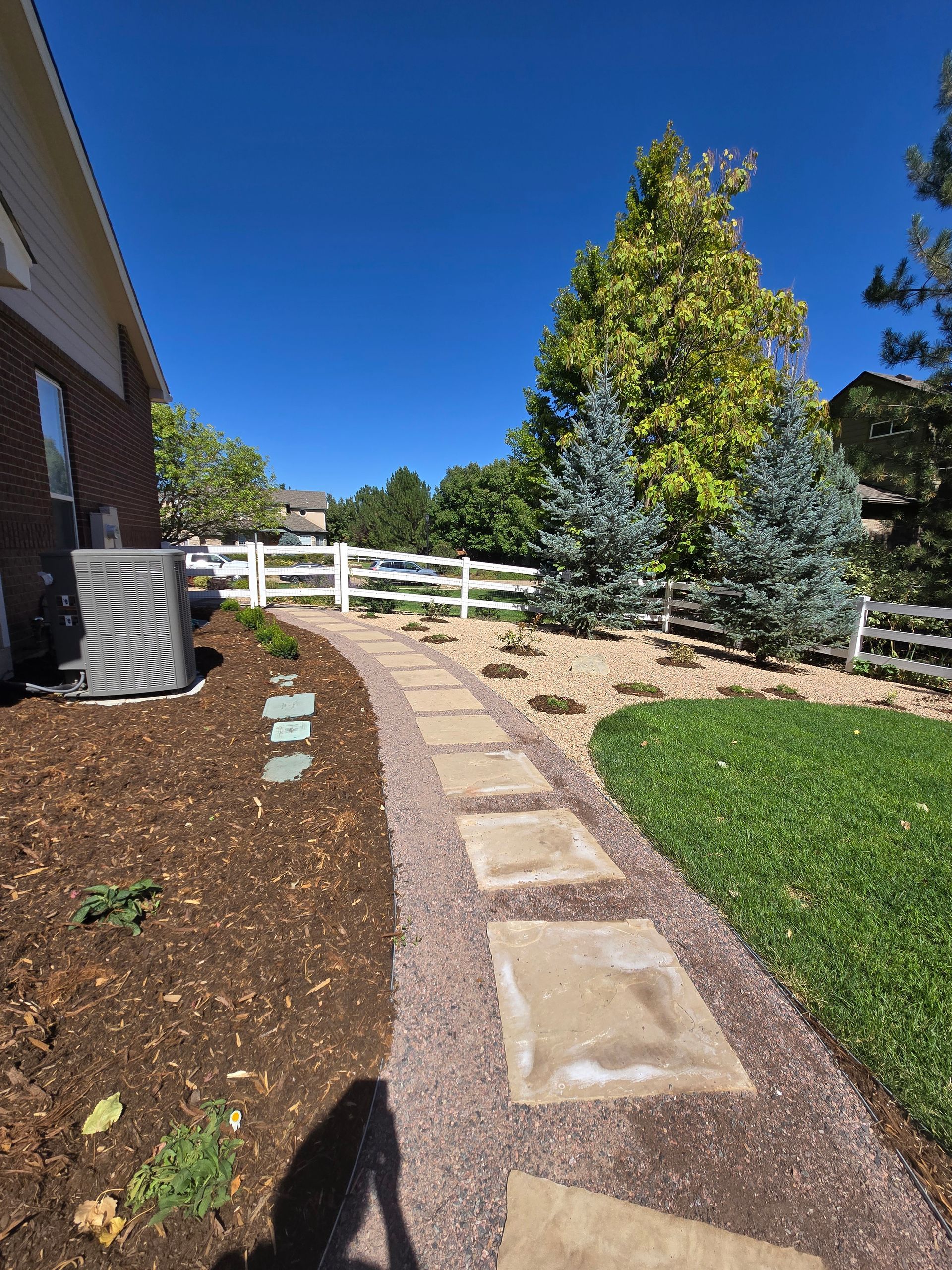 A stone walkway leading to a house with a white fence