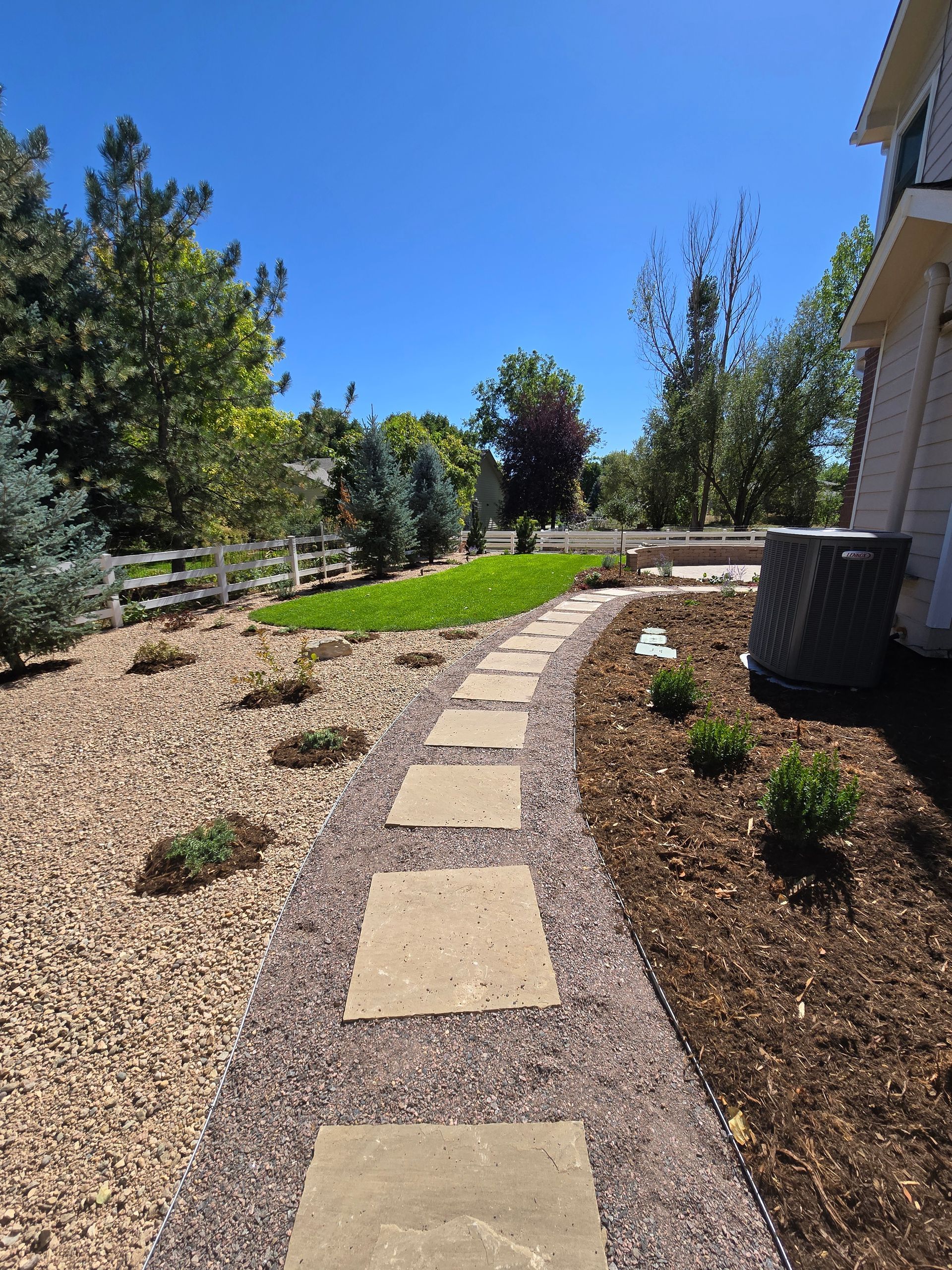 A stone walkway leading to a house with a fence in the background