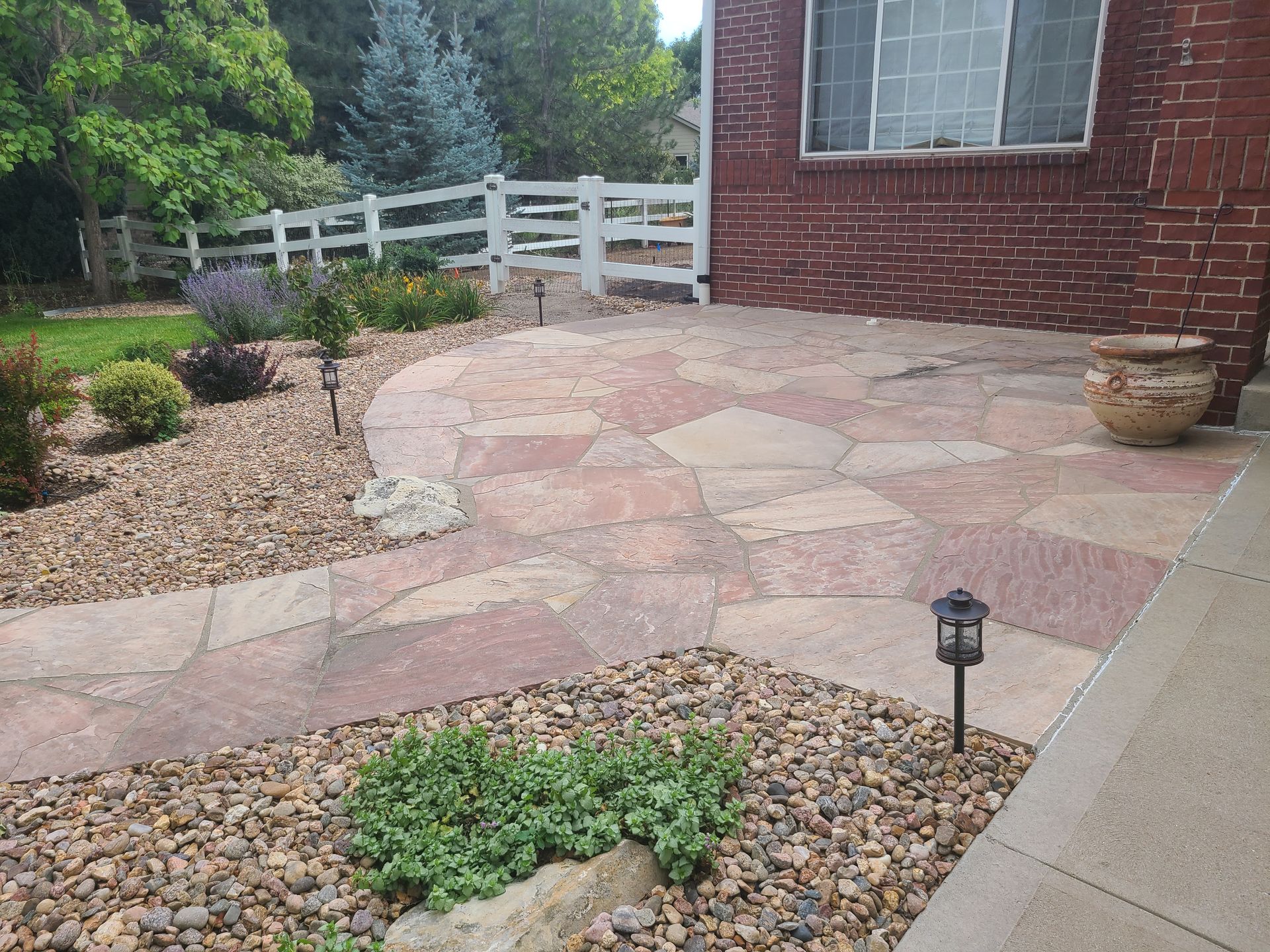 A stone walkway leading to a brick house with a white fence in the background