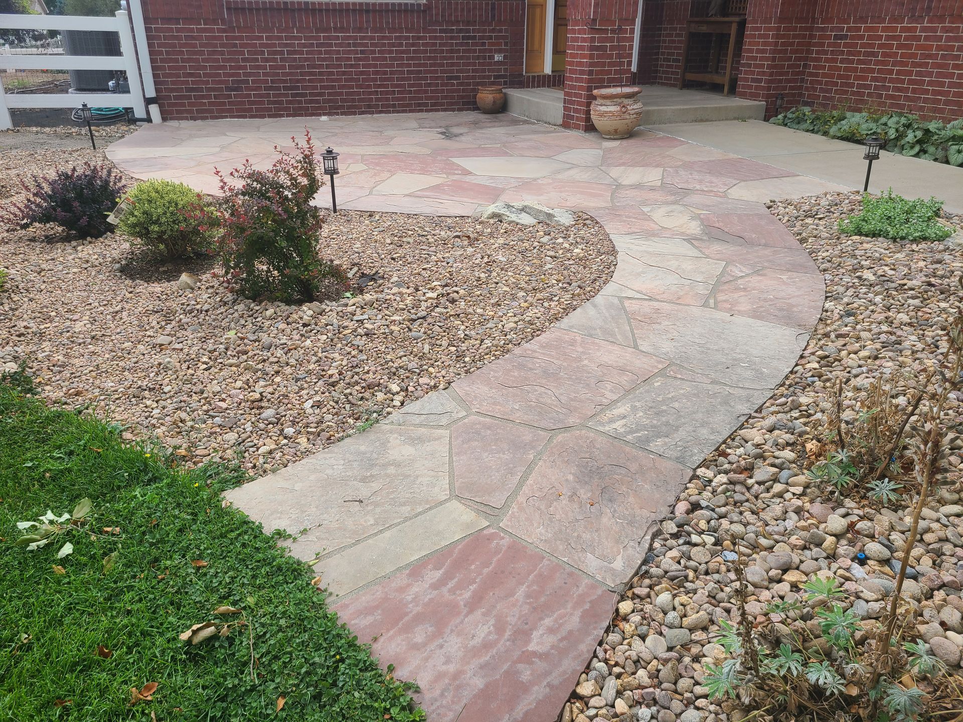 A stone walkway leading to a brick house surrounded by rocks and grass