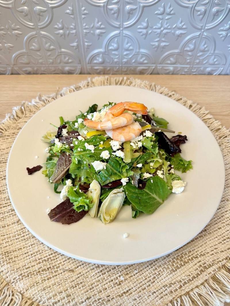 A white plate topped with a salad and shrimp on a table.