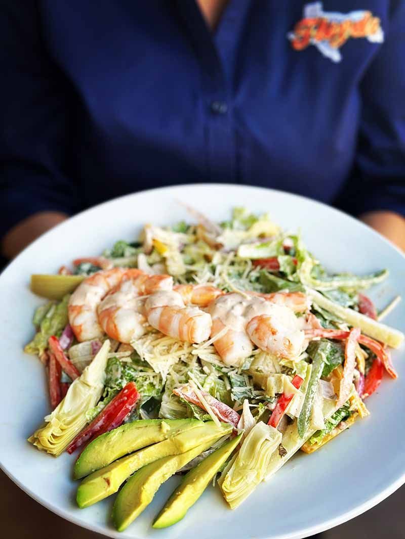 A person is holding a plate of food with shrimp and vegetables.