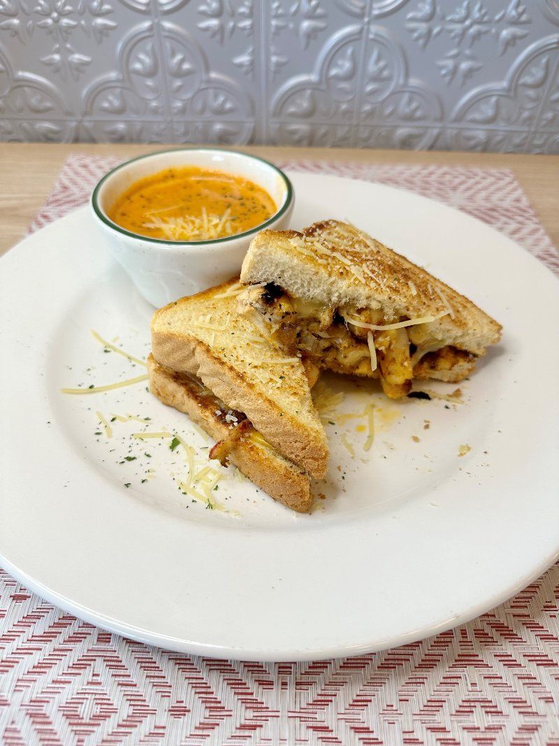 A grilled cheese sandwich and a bowl of soup on a white plate.