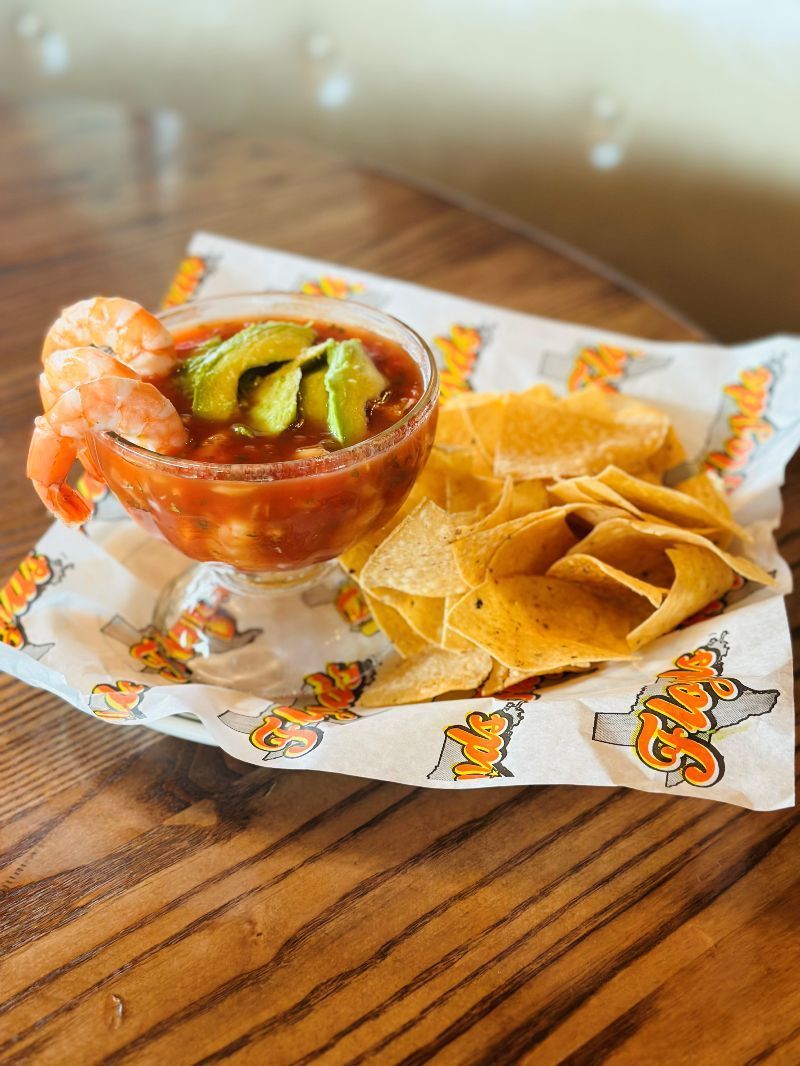 A bowl of shrimp cocktail and tortilla chips on a wooden table.