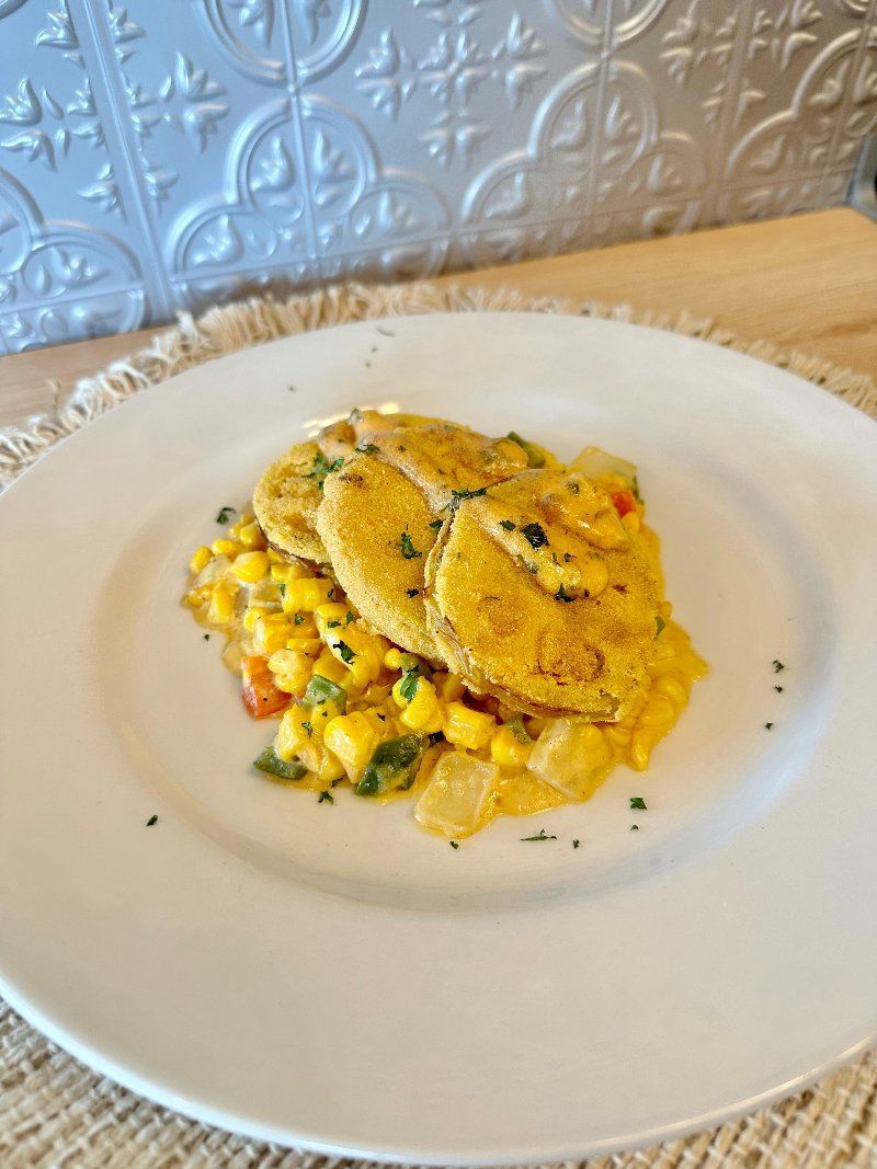 A white plate topped with chicken and corn on the cob on a table.