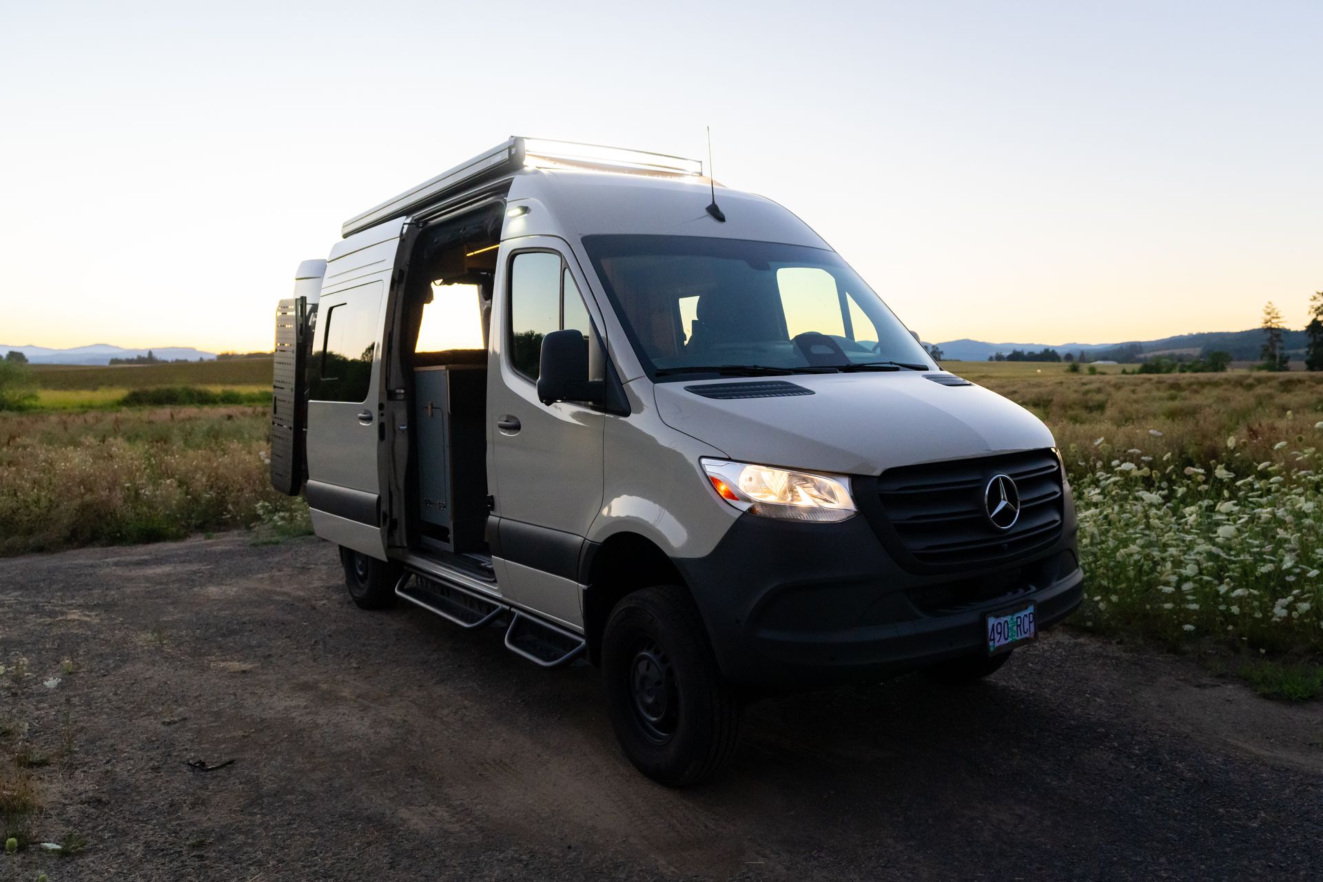 White Mercedes van parked on a dirt road at sunset, with open side door and black trim.