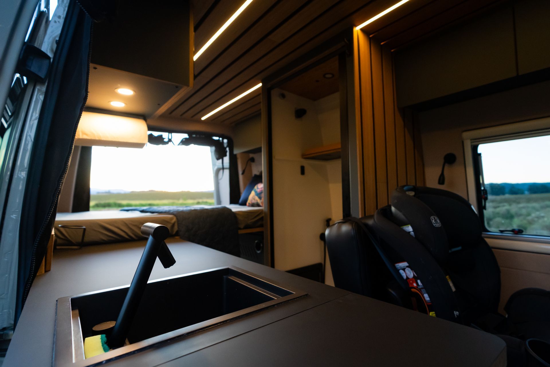 Cozy camper van interior with bed, wood ceiling lights, and large windows overlooking a landscape